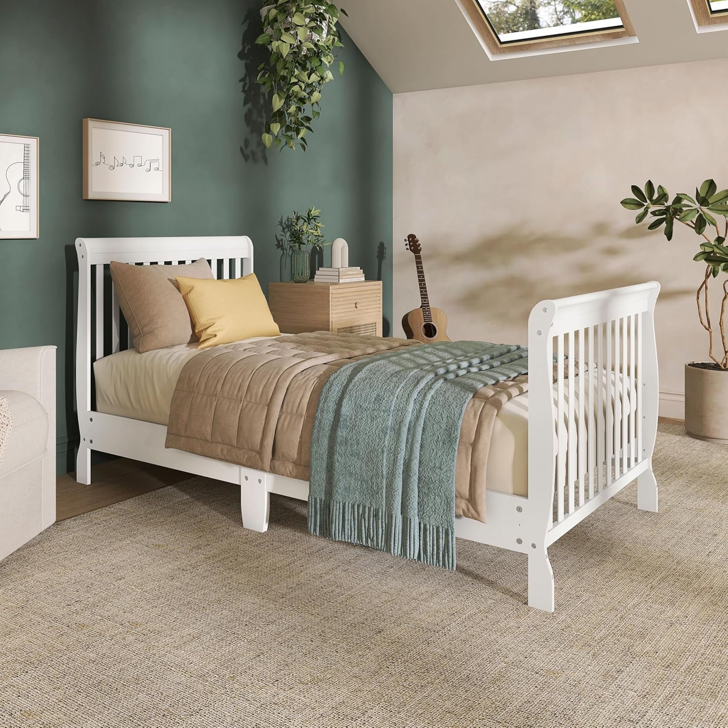 White mini crib set up as a toddler bed in a styled bedroom with green accent wall.