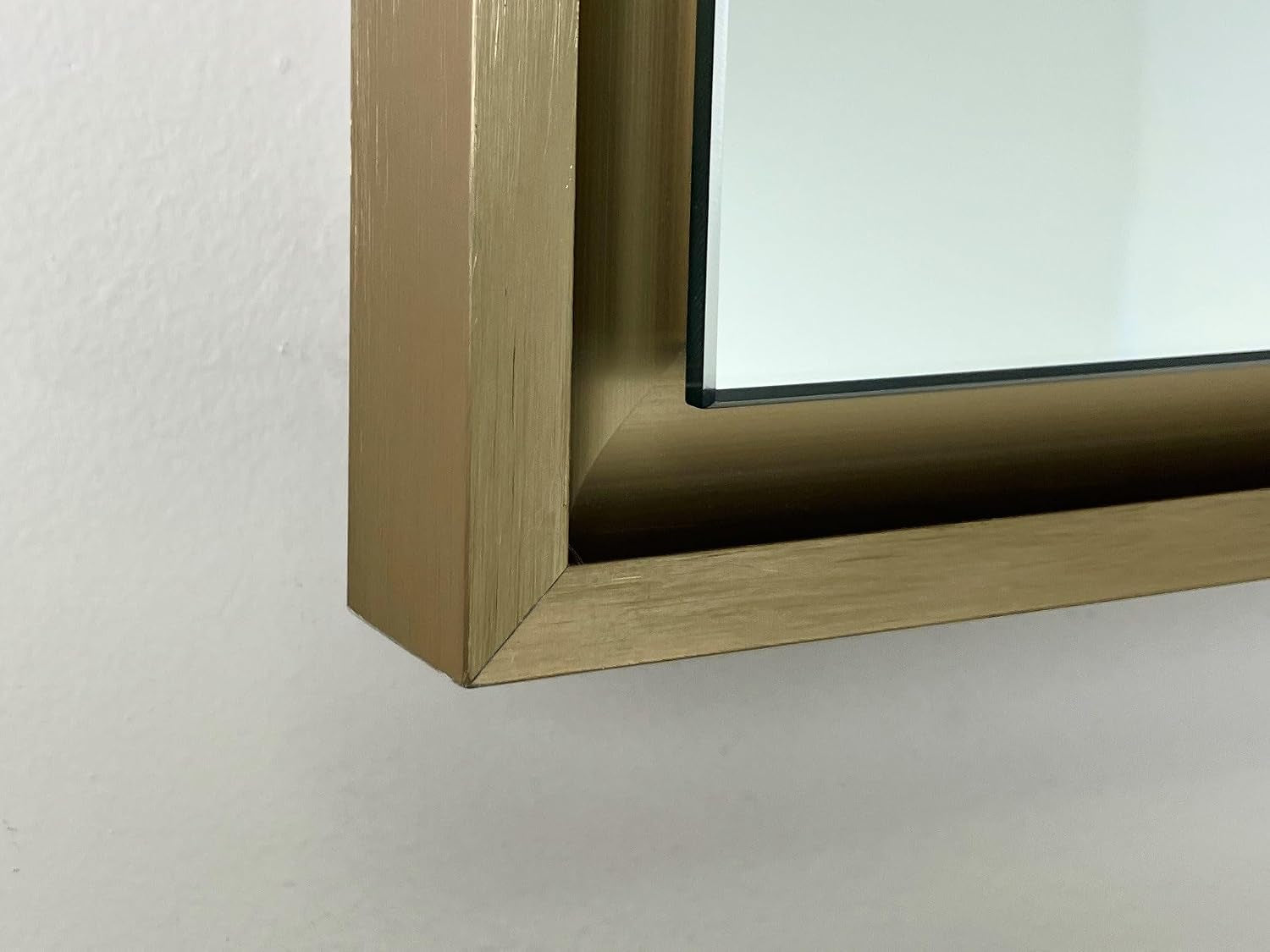 Close-up of the lower-left corner of a brushed gold metal mirror frame and mirrored edge