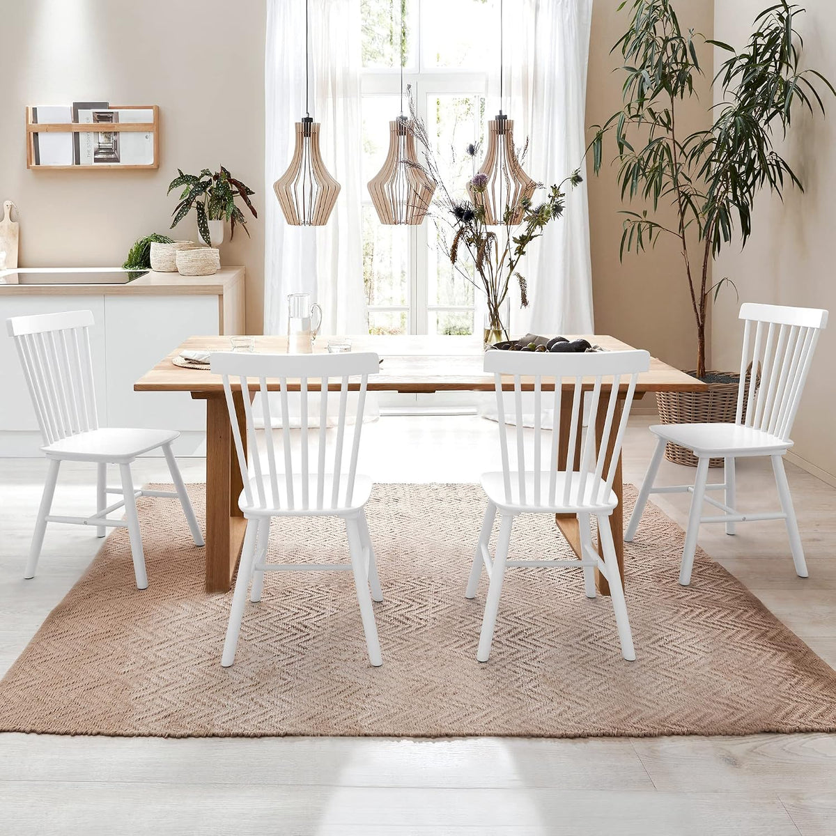 Set of four white spindle-back wooden chairs arranged around a wooden dining table in a bright room.