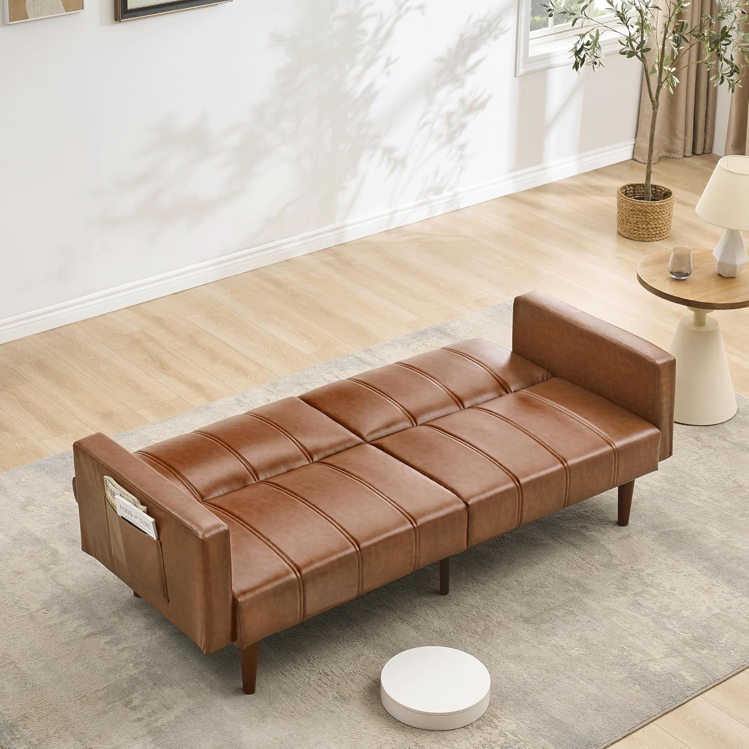 Brown PU leather futon shown fully flattened into a bed with visible side pocket on the armrest