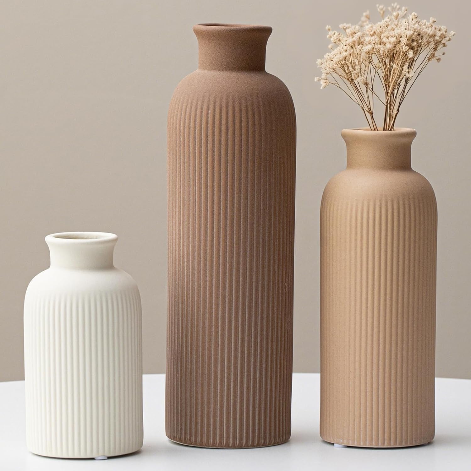 Three ribbed vases in cream, medium brown, and light terracotta standing side by side, one with dried blooms.