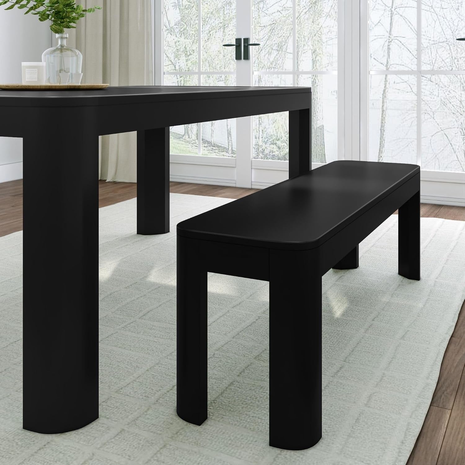 Close-up of a black dining table corner with matching rounded-edge bench on a light rug.