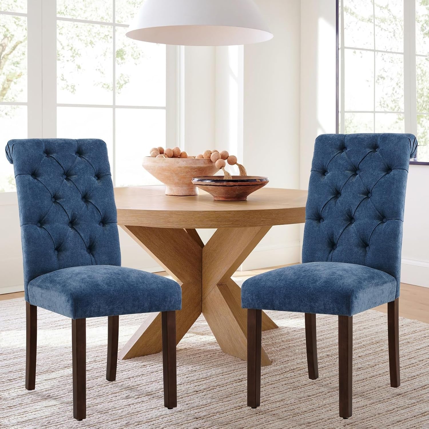 Pair of blue tufted dining chairs flanking a round wood table in a bright windowed dining nook