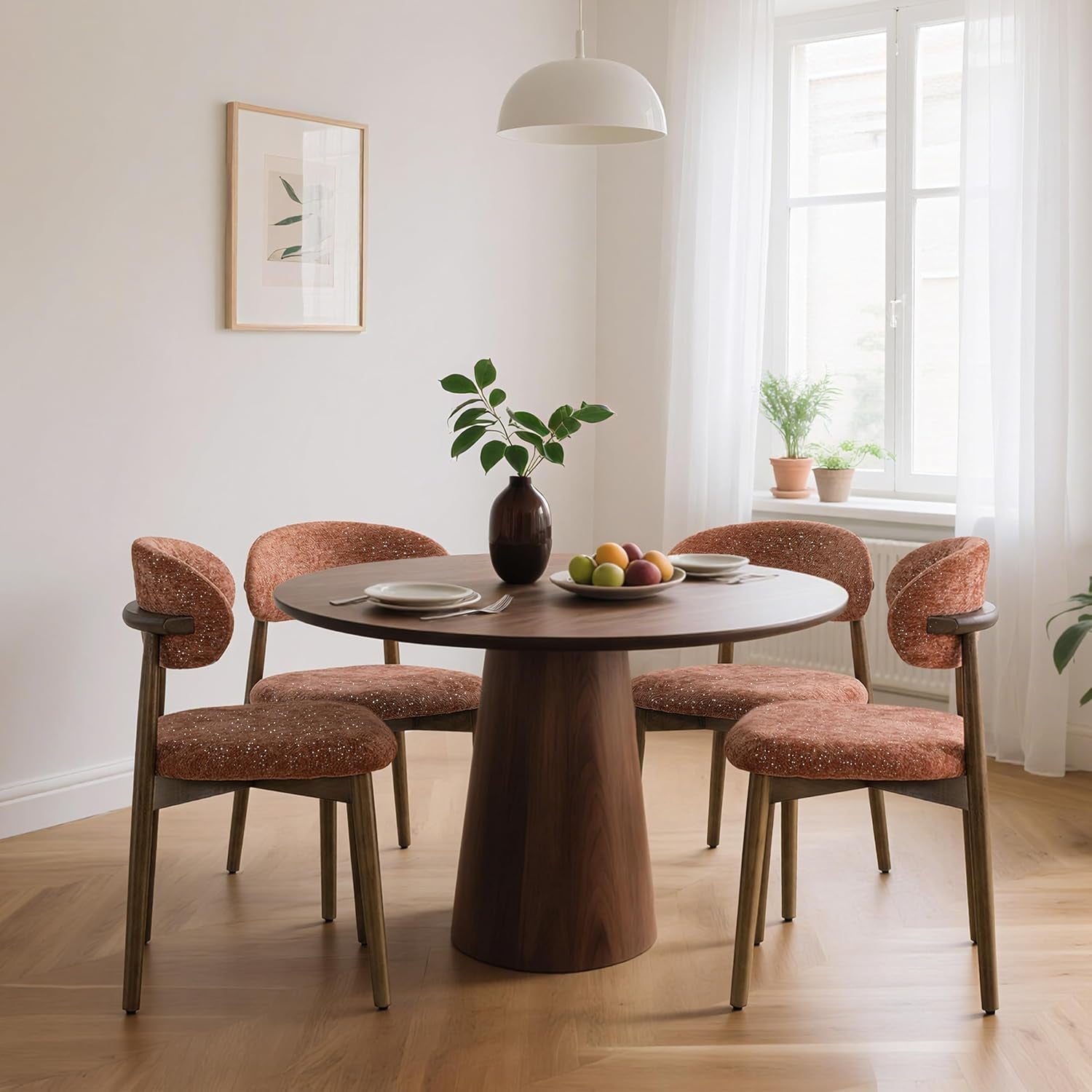 Four rust upholstered dining chairs with curved backs surround a round table in a bright dining room.