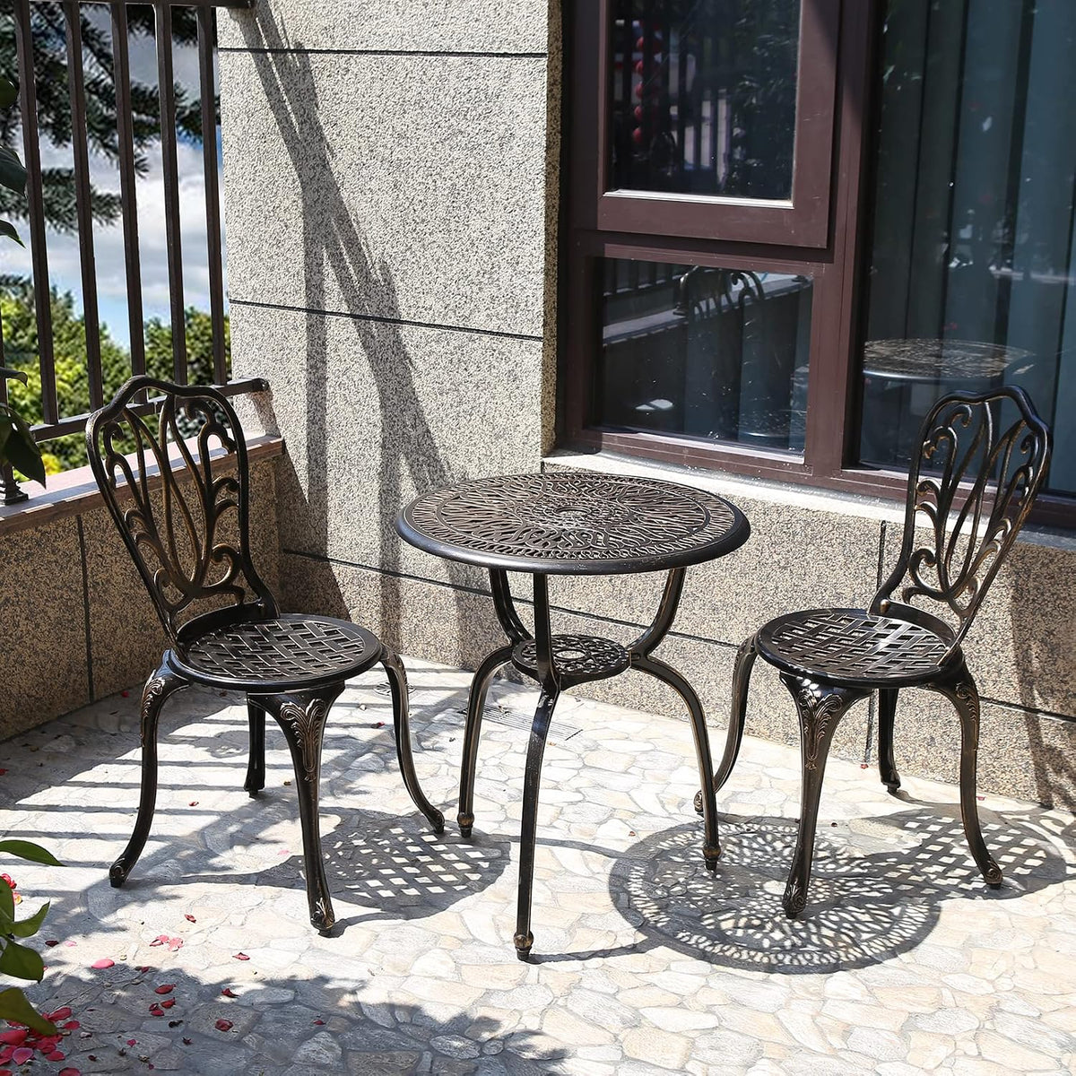 Patio view of the cast aluminum bistro set in dark bronze finish beside a window and railing.