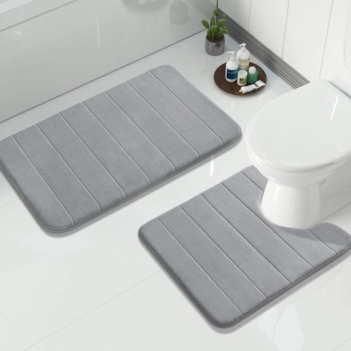 Gray bathroom mats positioned beside a toilet with a small tray of bottles on the floor.