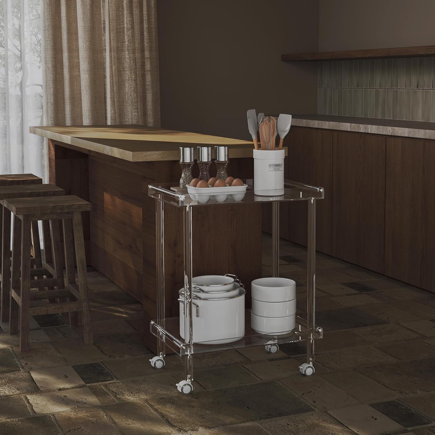 Clear acrylic two-tier cart in a kitchen beside an island, stocked with bowls, pots, eggs and a utensil holder.