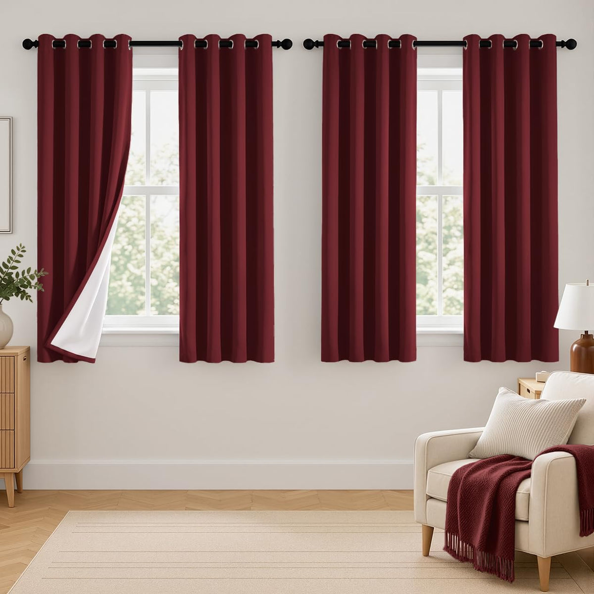 Three windows dressed with deep burgundy grommet curtains, leftmost panel folded to reveal white lining