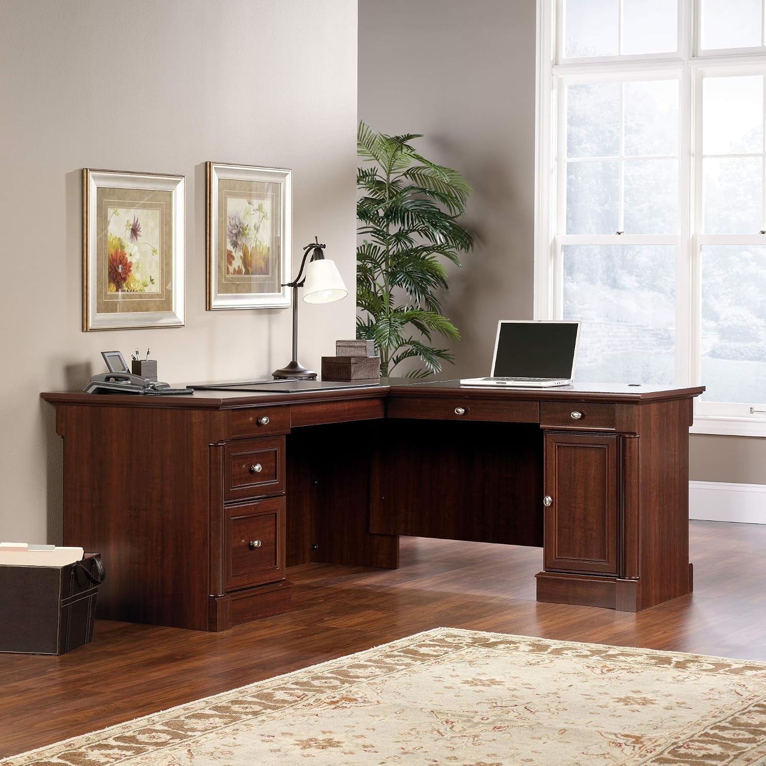 L-shaped desk in dark cherry shown in a room with lamp and accessories, front-right angled view