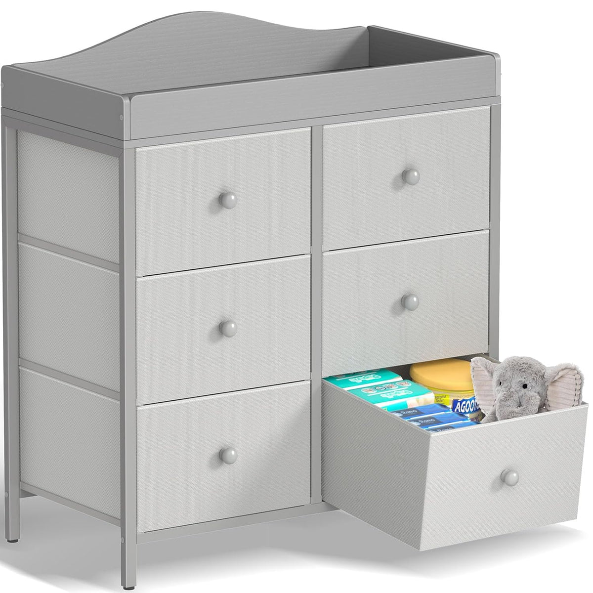 Light gray six-drawer changing dresser with one lower drawer open revealing diapers and a plush elephant.