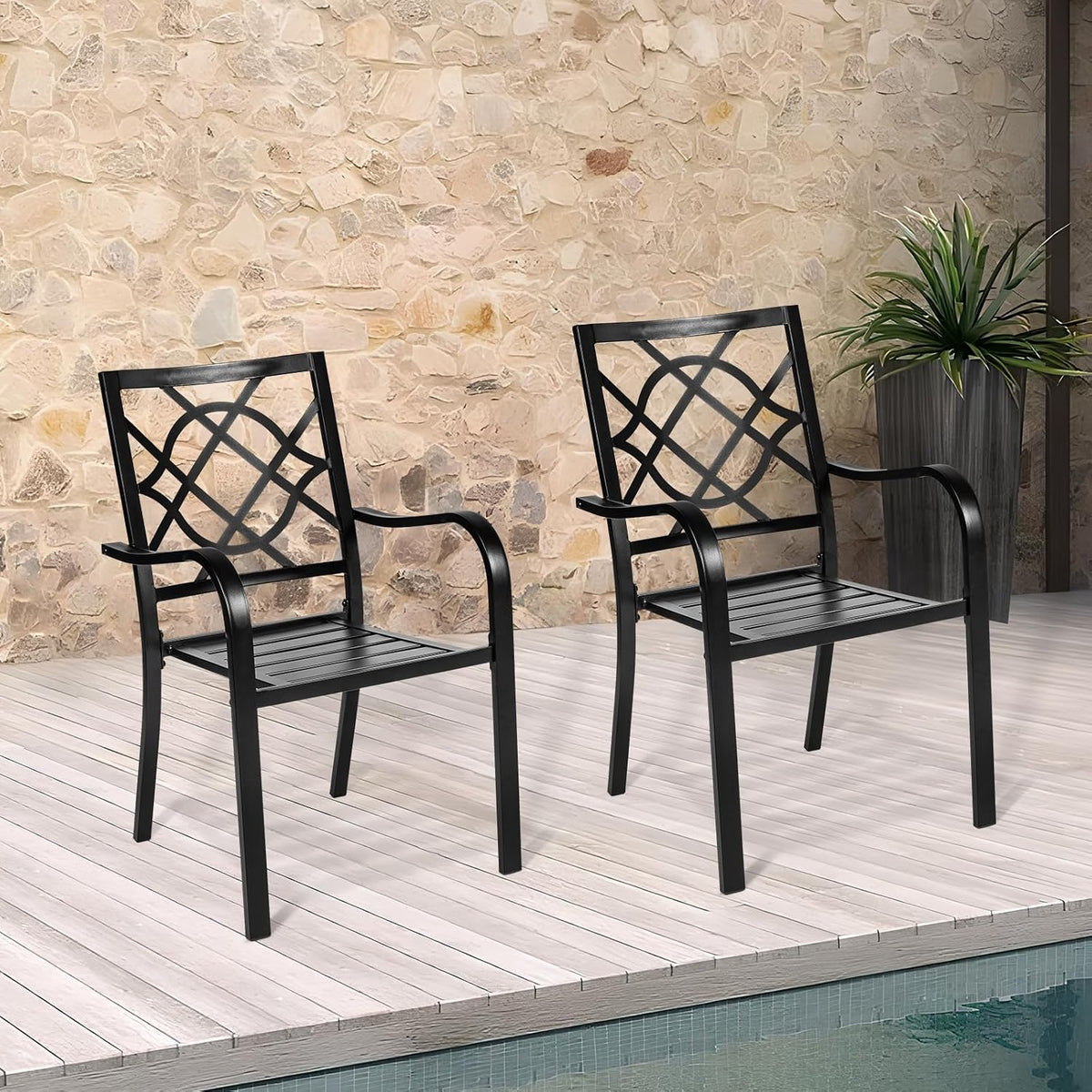 Two black metal chairs with lattice backs on a light wood deck in front of a stone wall and tall planter