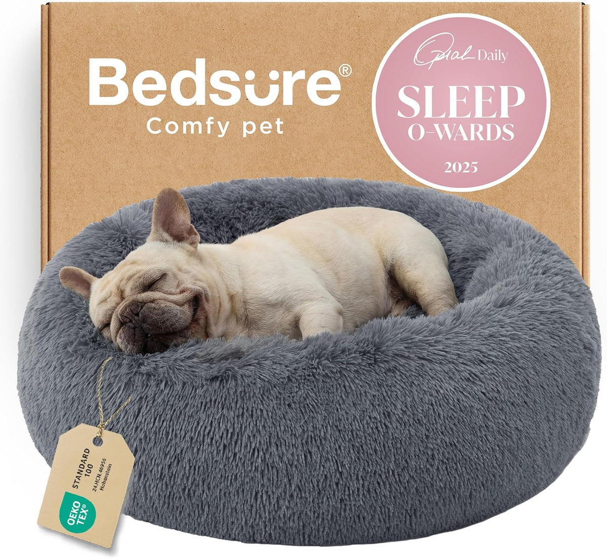 Close-up front view of a cream French bulldog sleeping in a gray fluffy round bed with a hanging product tag and boxed