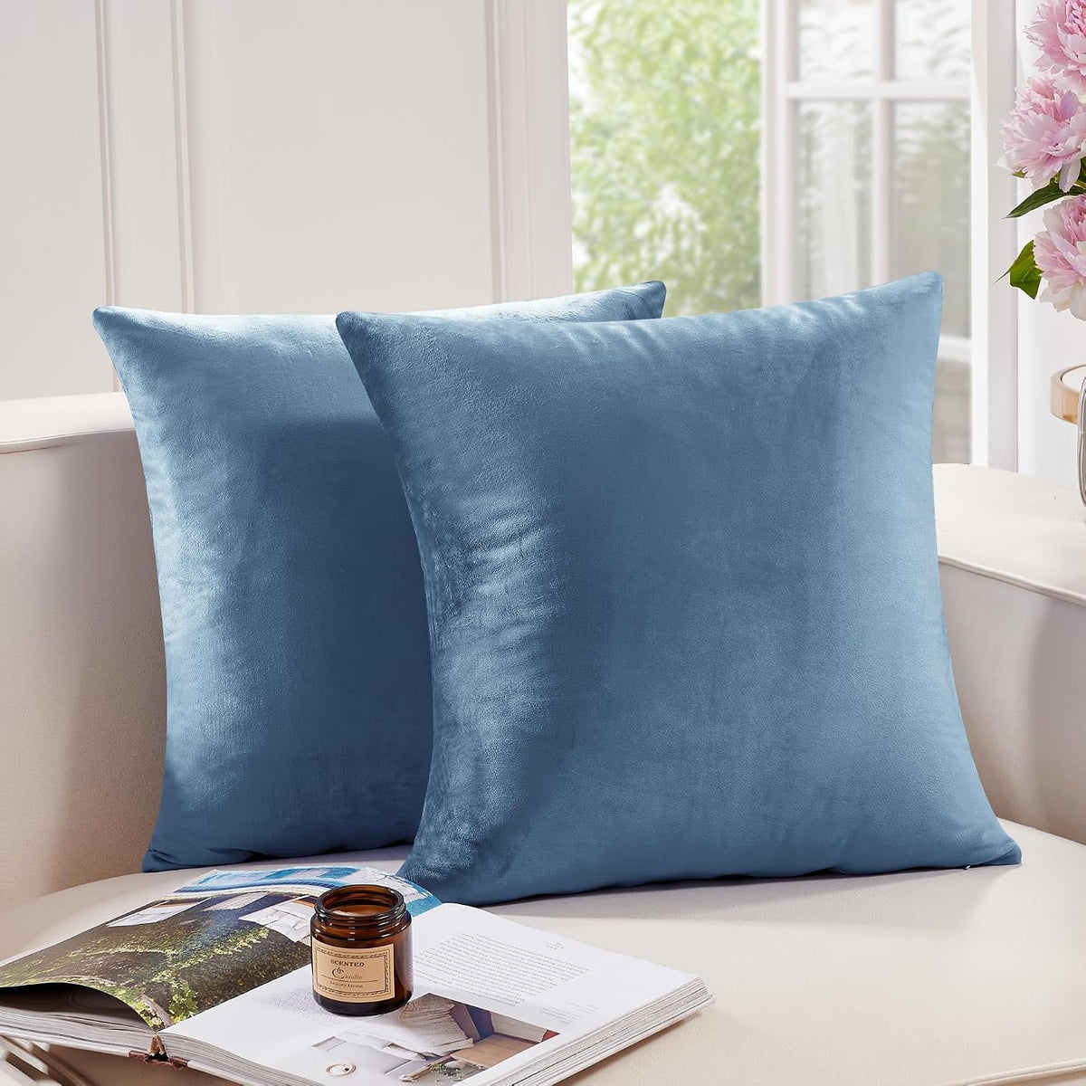 Two blue square throw pillow covers styled on a light sofa beside a window and open magazine with a candle.