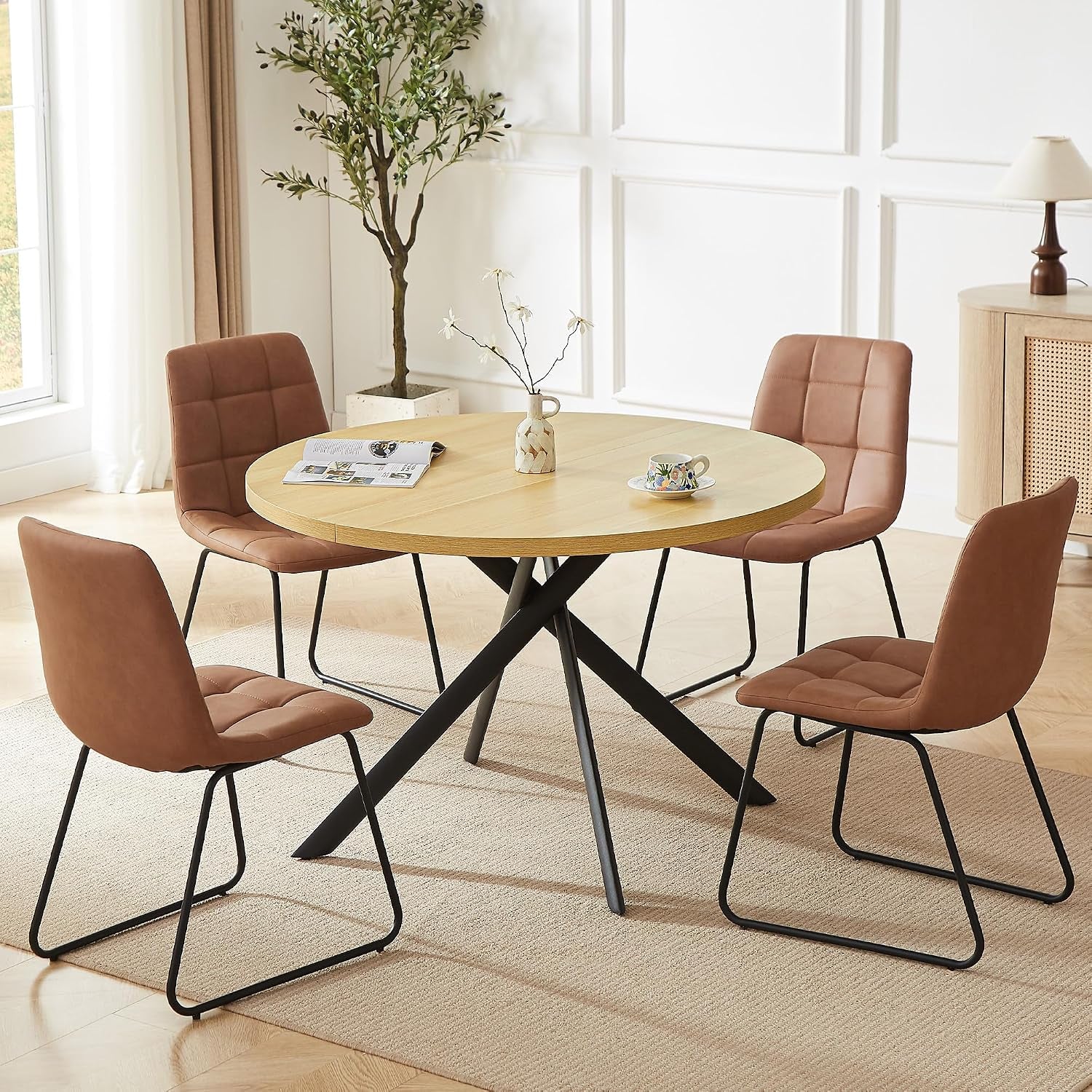 Round light-wood table with four brown padded chairs and black sled-style legs on a rug