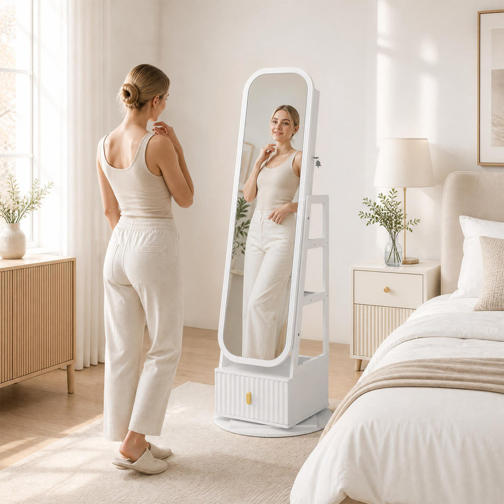 A woman looks in a white full-length mirror cabinet in a softly lit bedroom.
