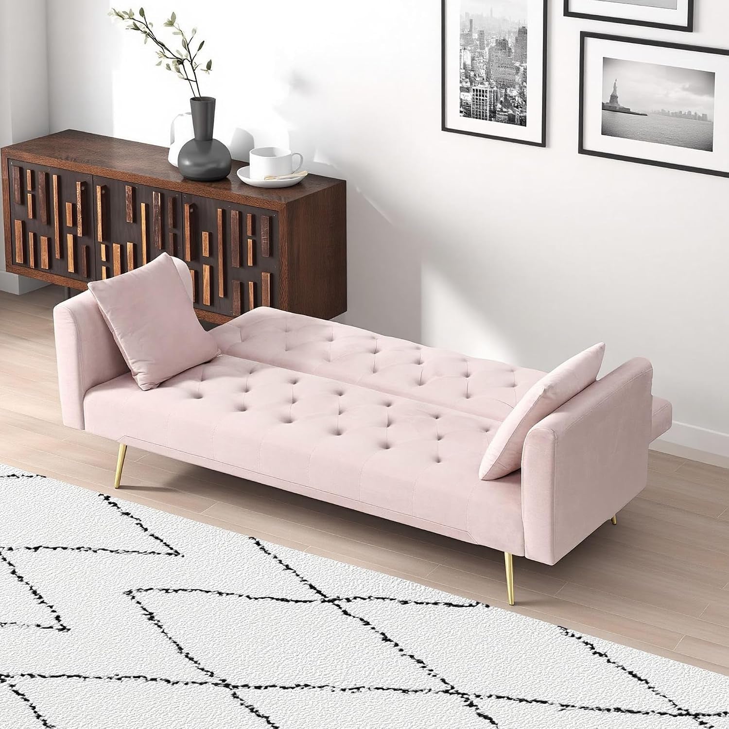 Light pink futon sofa converted flat into bed with tufted surface and two pillows in a room setting