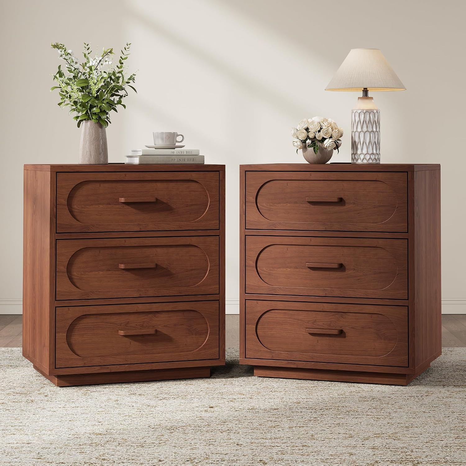 Pair of warm brown three-drawer nightstands side by side with lamps and decorative items on top.
