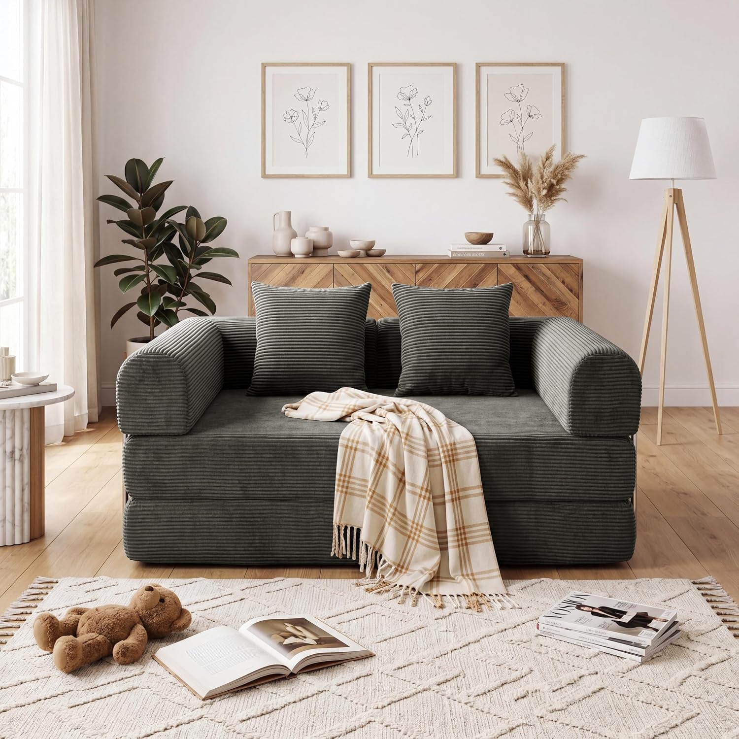 Front view of a charcoal gray corduroy convertible sofa with two pillows and a plaid throw draped over the seat.