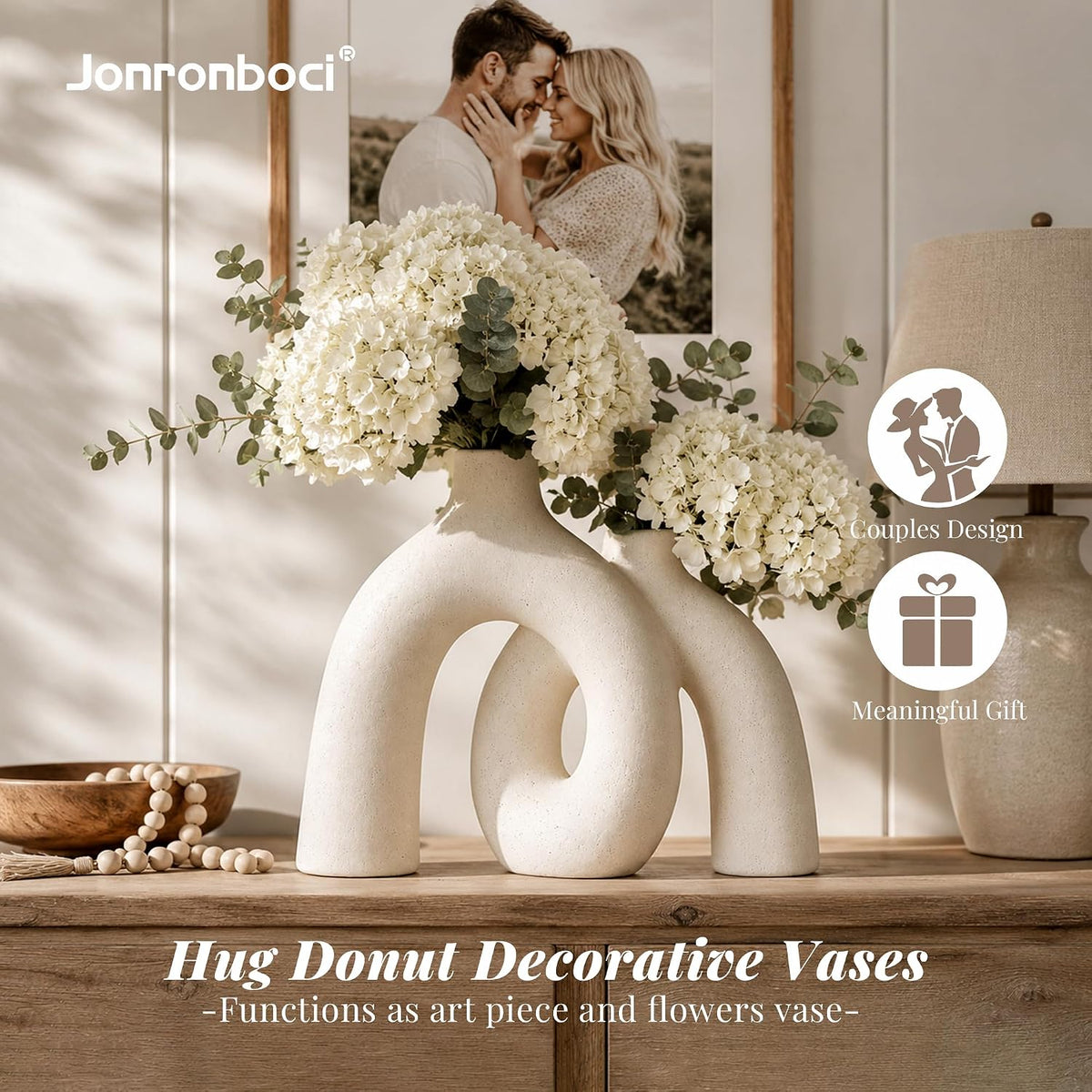Cream ceramic donut vase styled with white hydrangeas on a wooden console among framed art and tabletop decor