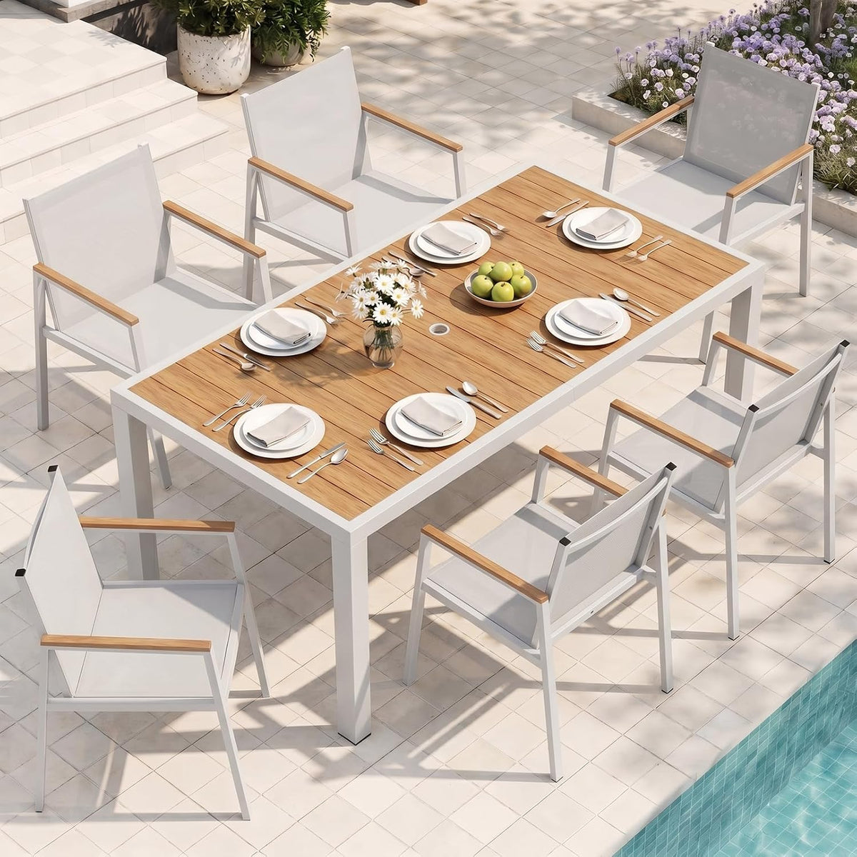 Aerial view of a white-framed outdoor dining table with light wood top and six white armchairs by a pool.