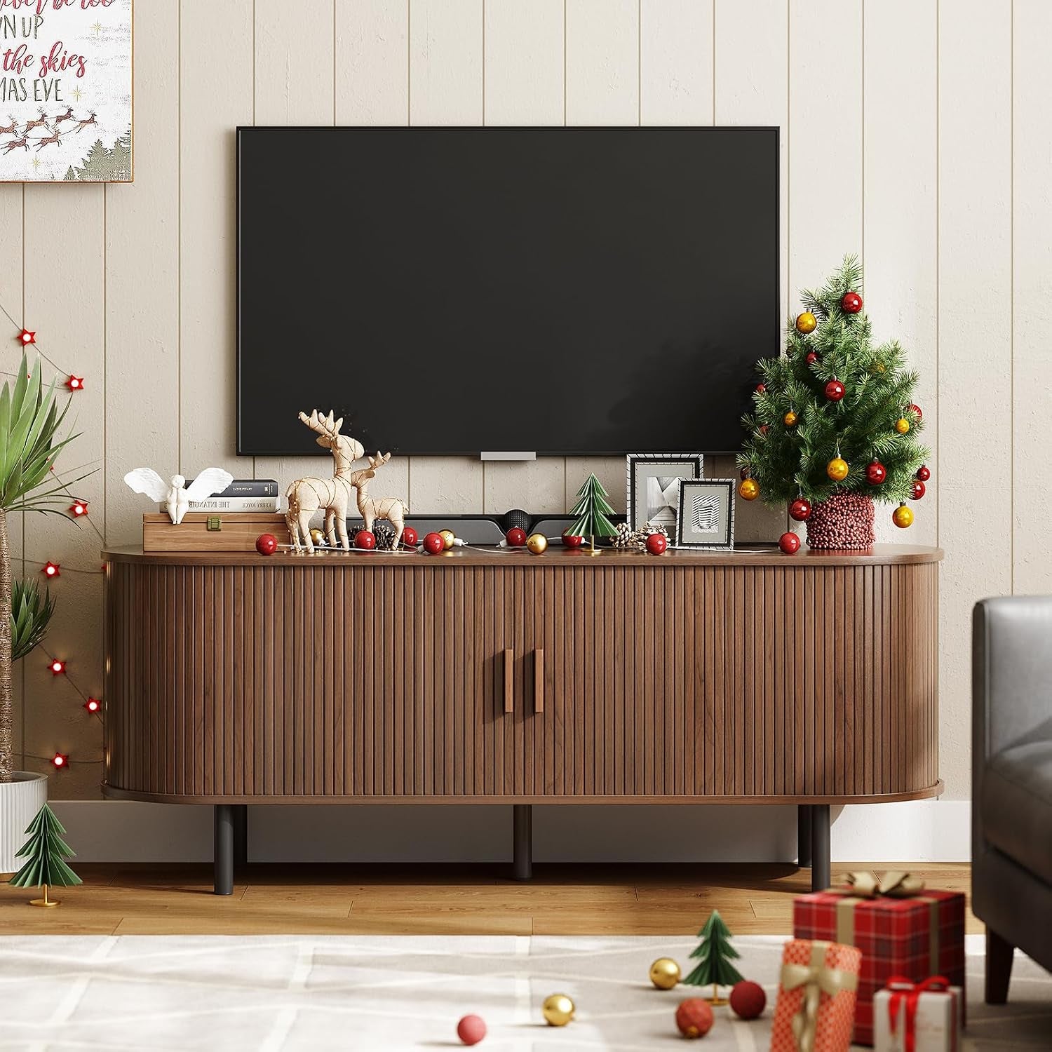 Darker walnut ribbed TV stand decorated with a small Christmas tree, reindeer figures and scattered ornaments.