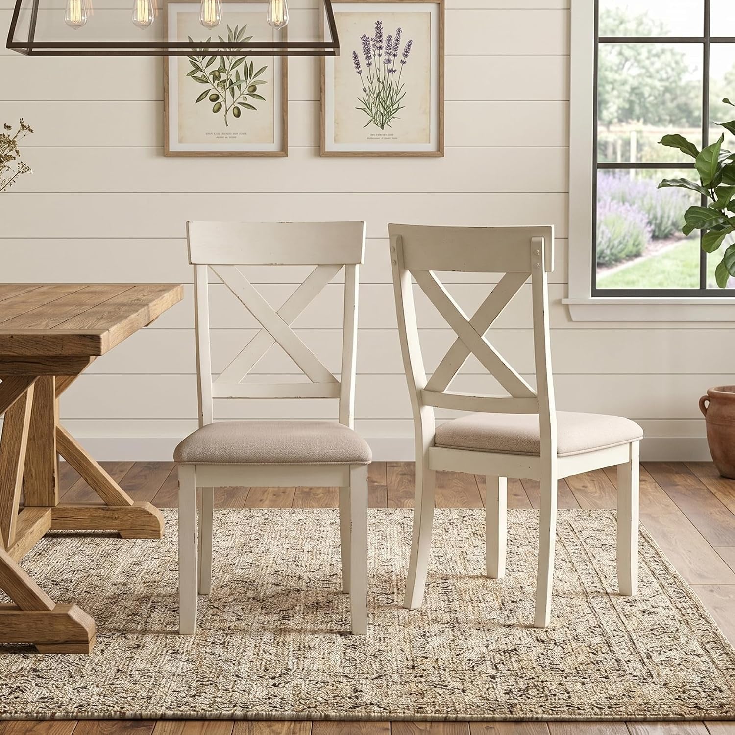 Two cross-back dining chairs with cushioned seats shown next to a partial view of a wooden trestle table.