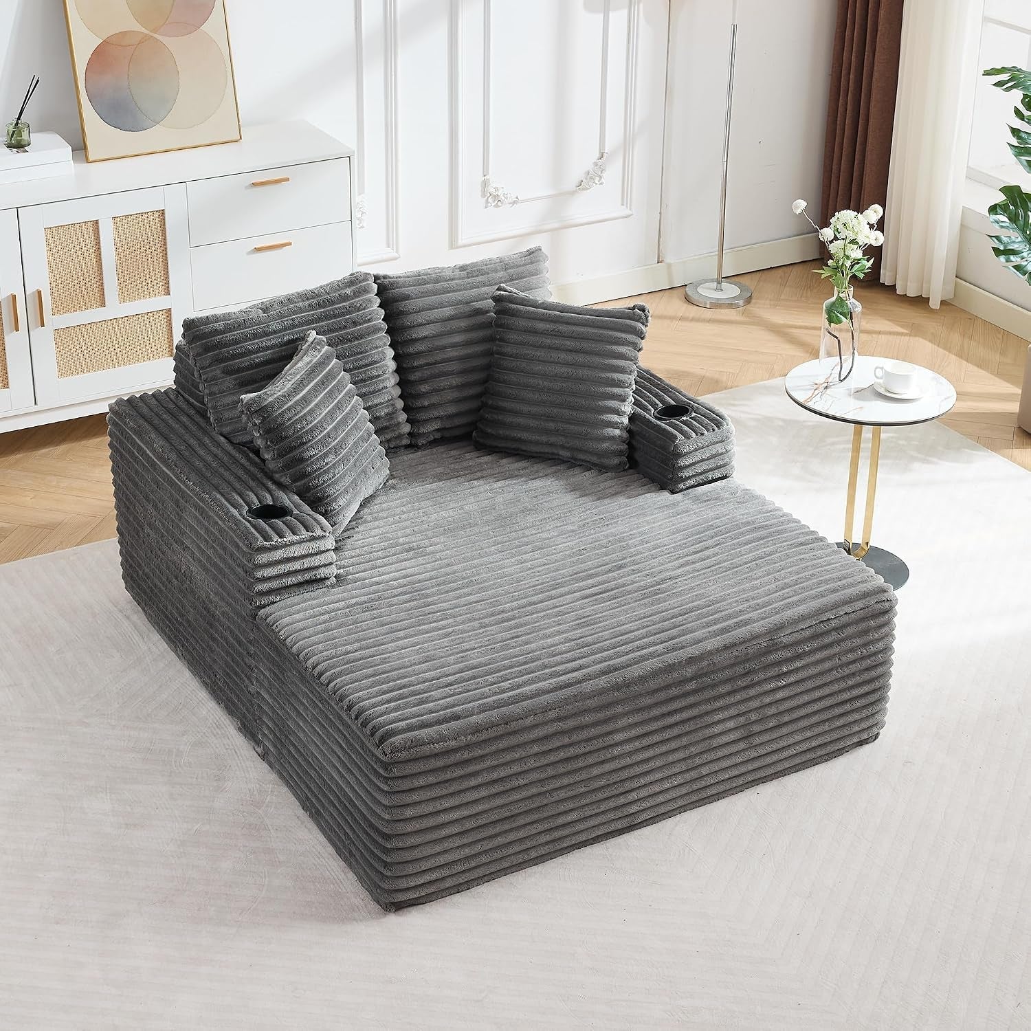 Empty oversized gray corduroy chaise with ribbed texture, pillows, and built-in cup holders in a styled living room.