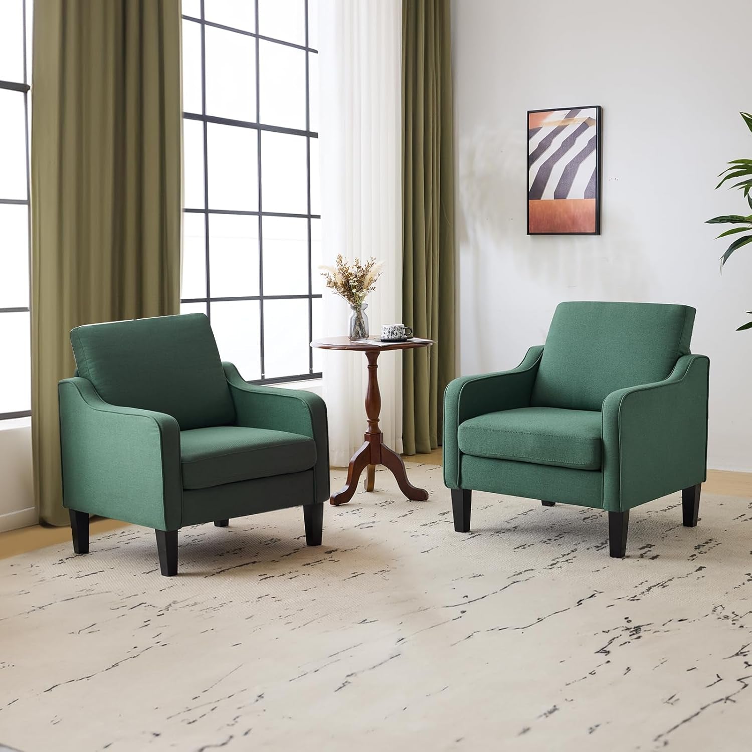 Two deep green upholstered armchairs with black wooden legs flanking a small round table.