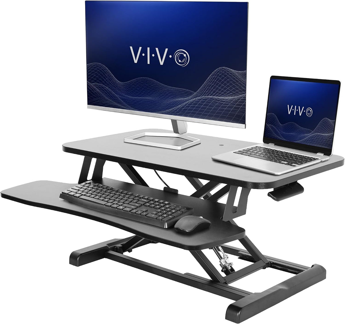 Angled view of a gray standing desk converter with monitor, laptop, keyboard and mouse arranged on shelves
