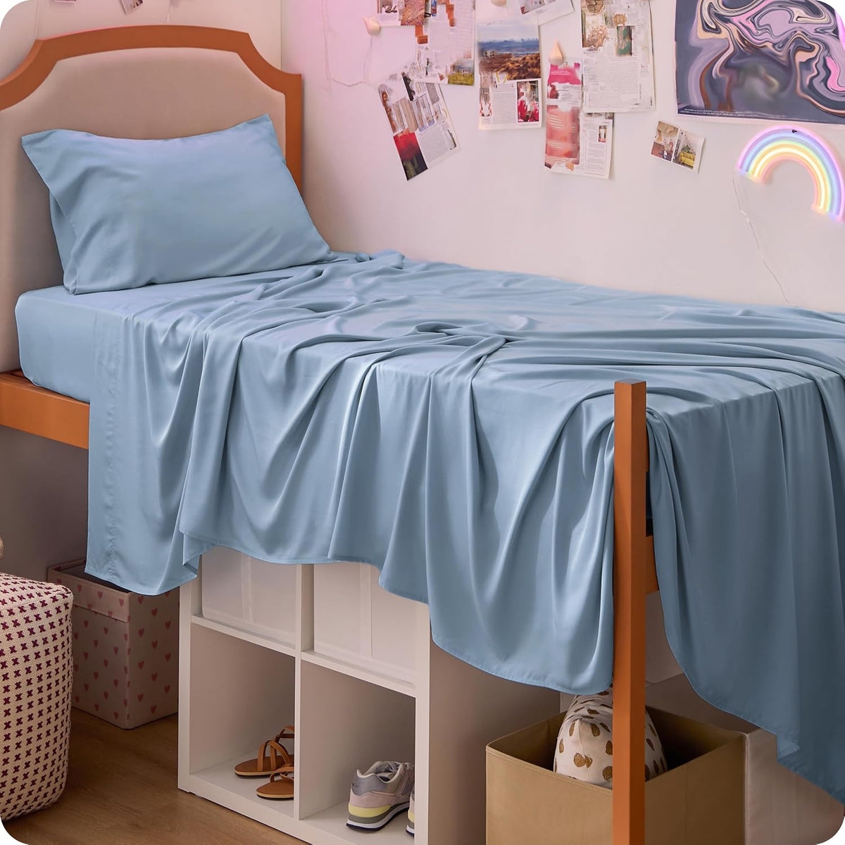 Side view of a single loft-style bed with light blue sheets and a matching pillow, fabric draping over the frame and white