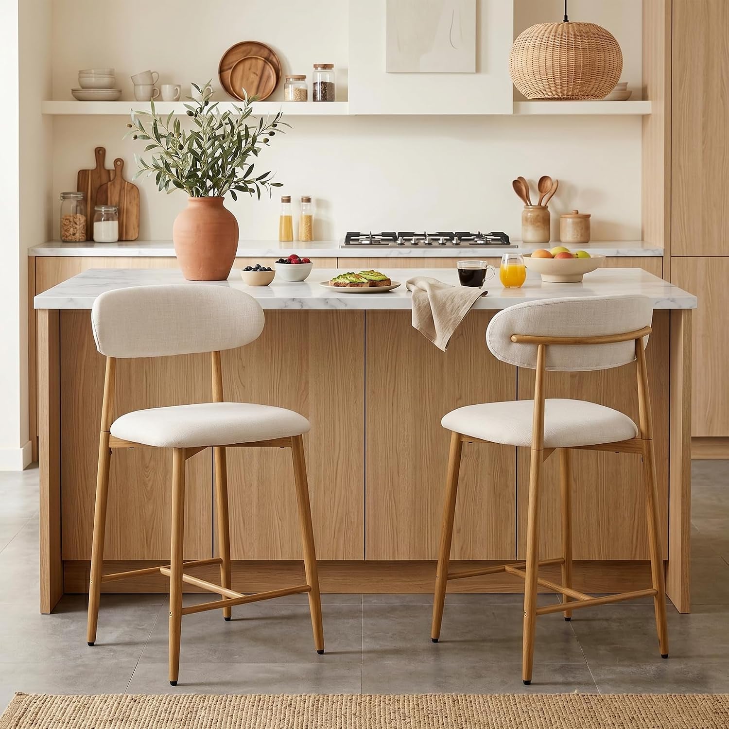 Front view of two beige upholstered counter stools at a kitchen island, rounded backs and metal legs visible.
