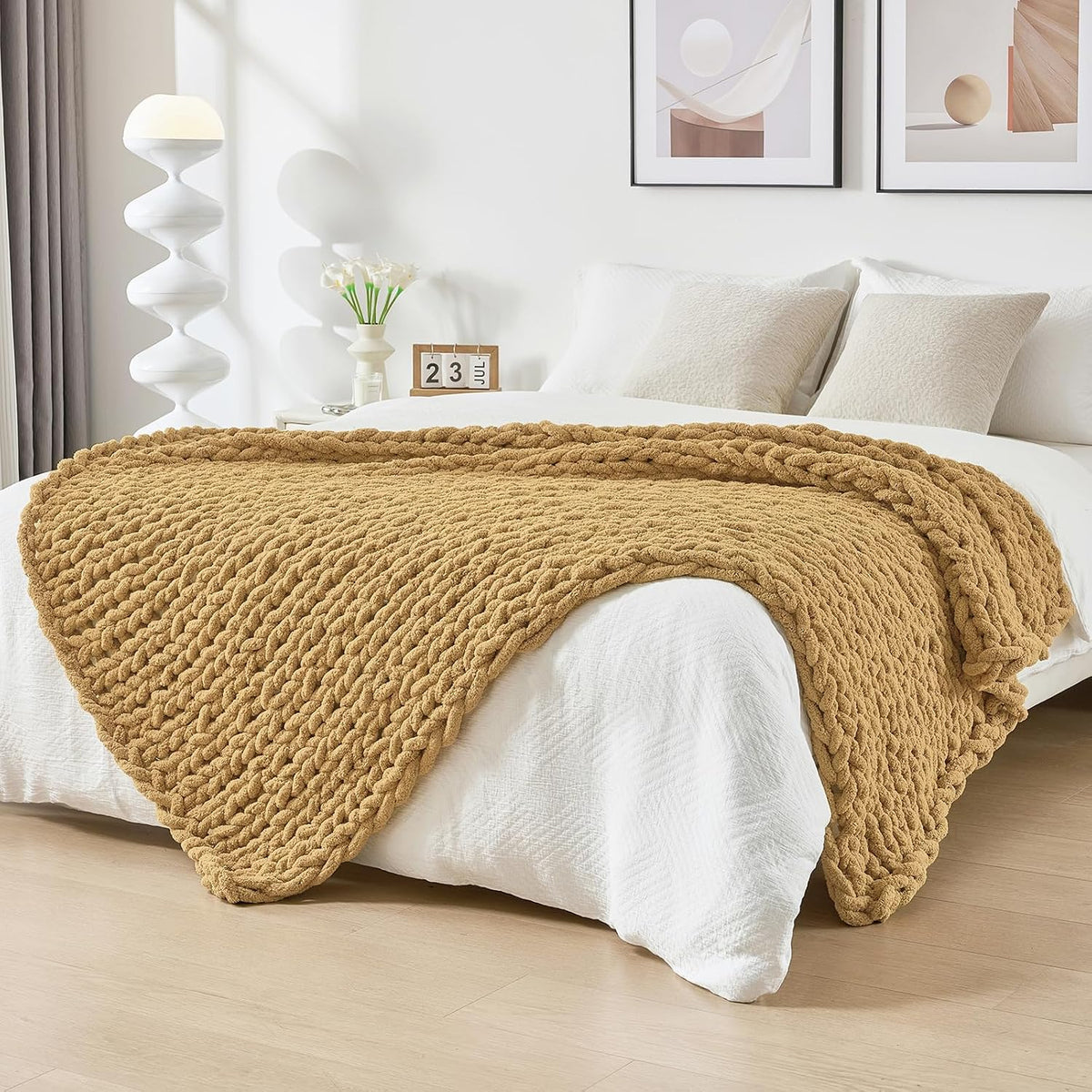 Warm mustard-colored chunky knit throw spread across a white bed in a bright bedroom