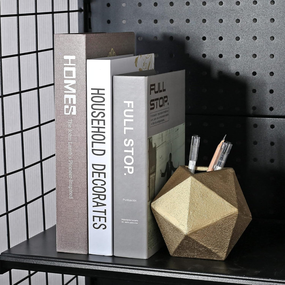Close-up of a gold geometric ball used as a pen holder beside upright books on a black pegboard shelf