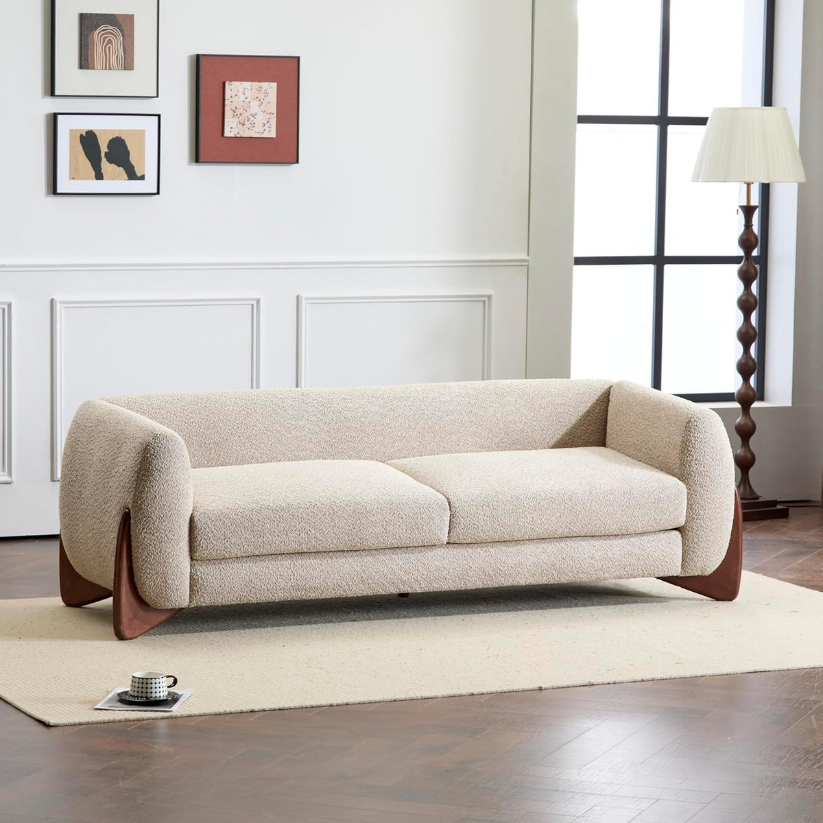 Cream boucle three-seat sofa with rounded arms and sculpted wooden legs on a light area rug.