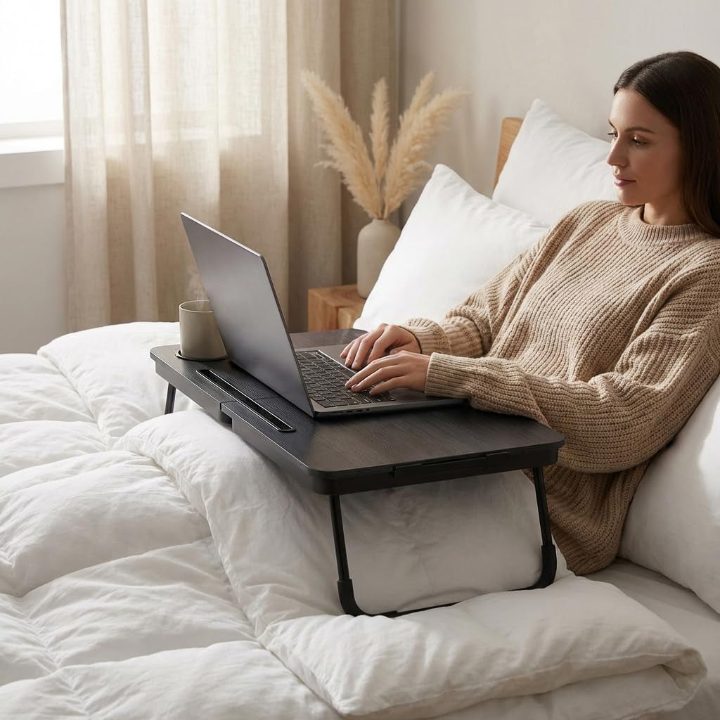 Person reclining on a bed using the black lap desk with a laptop positioned on the surface