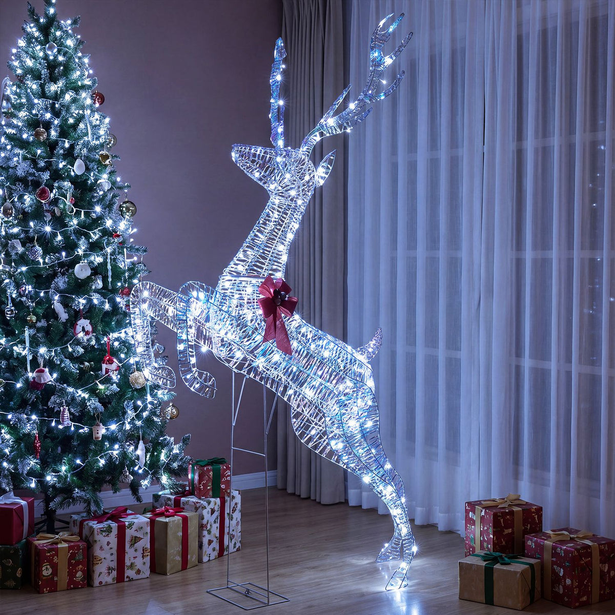 A glowing leaping reindeer decoration stands beside a decorated Christmas tree and wrapped gifts.