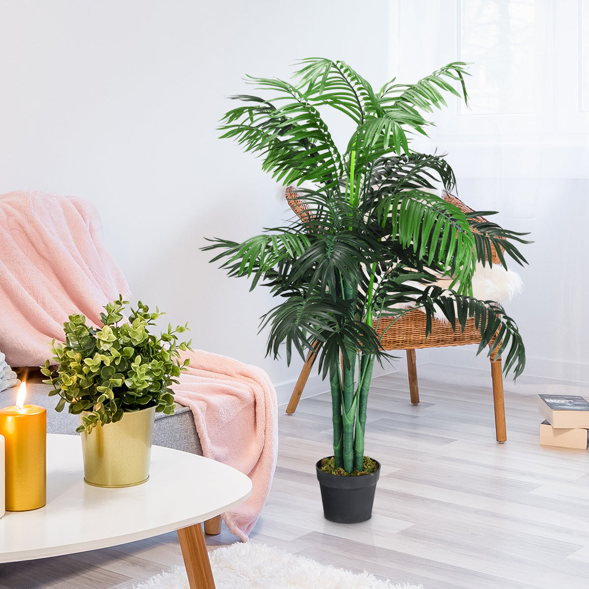 A leafy artificial palm stands near a white coffee table and pink-draped chair in a light room.