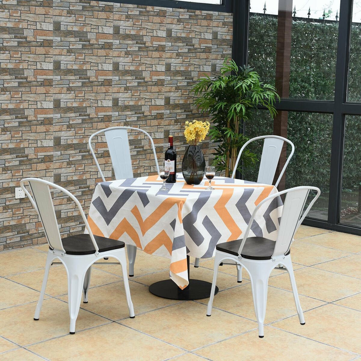 White metal chairs with dark seats surround a table covered in a patterned cloth on a tiled patio.