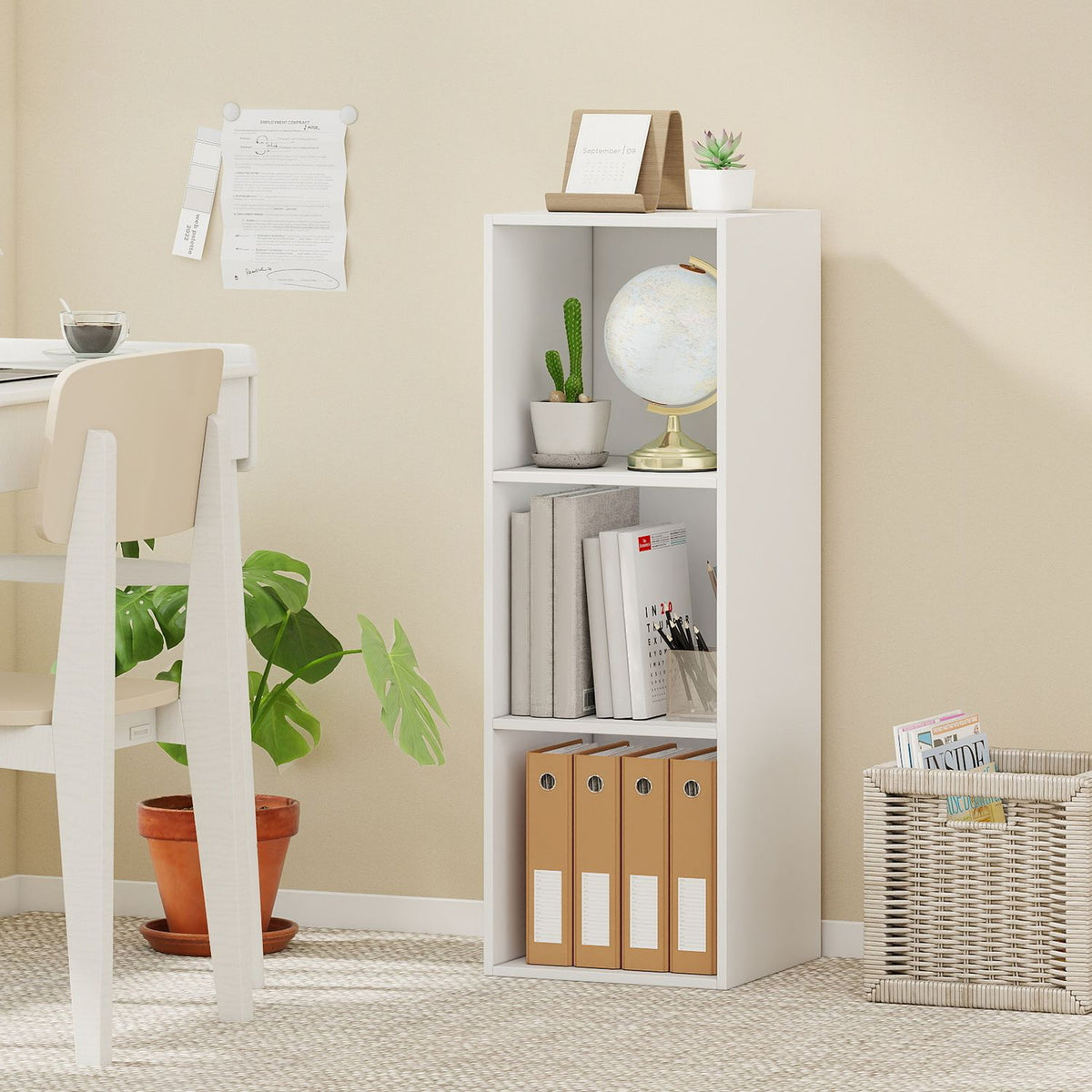 White three-cube bookshelf beside a desk, styled with books, a globe, plants and storage boxes.