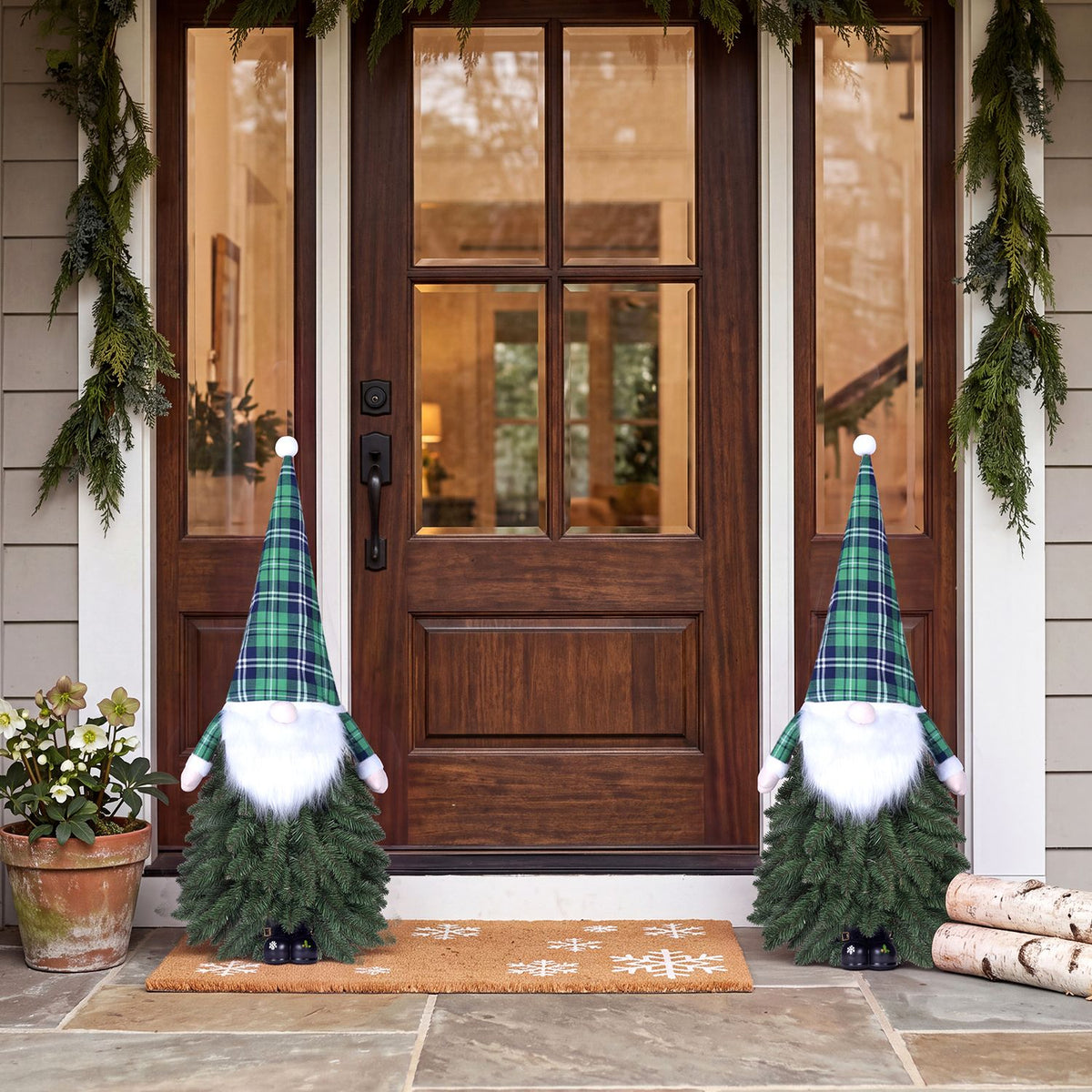 Two small evergreen gnome decorations stand on a porch beside a wooden front door.