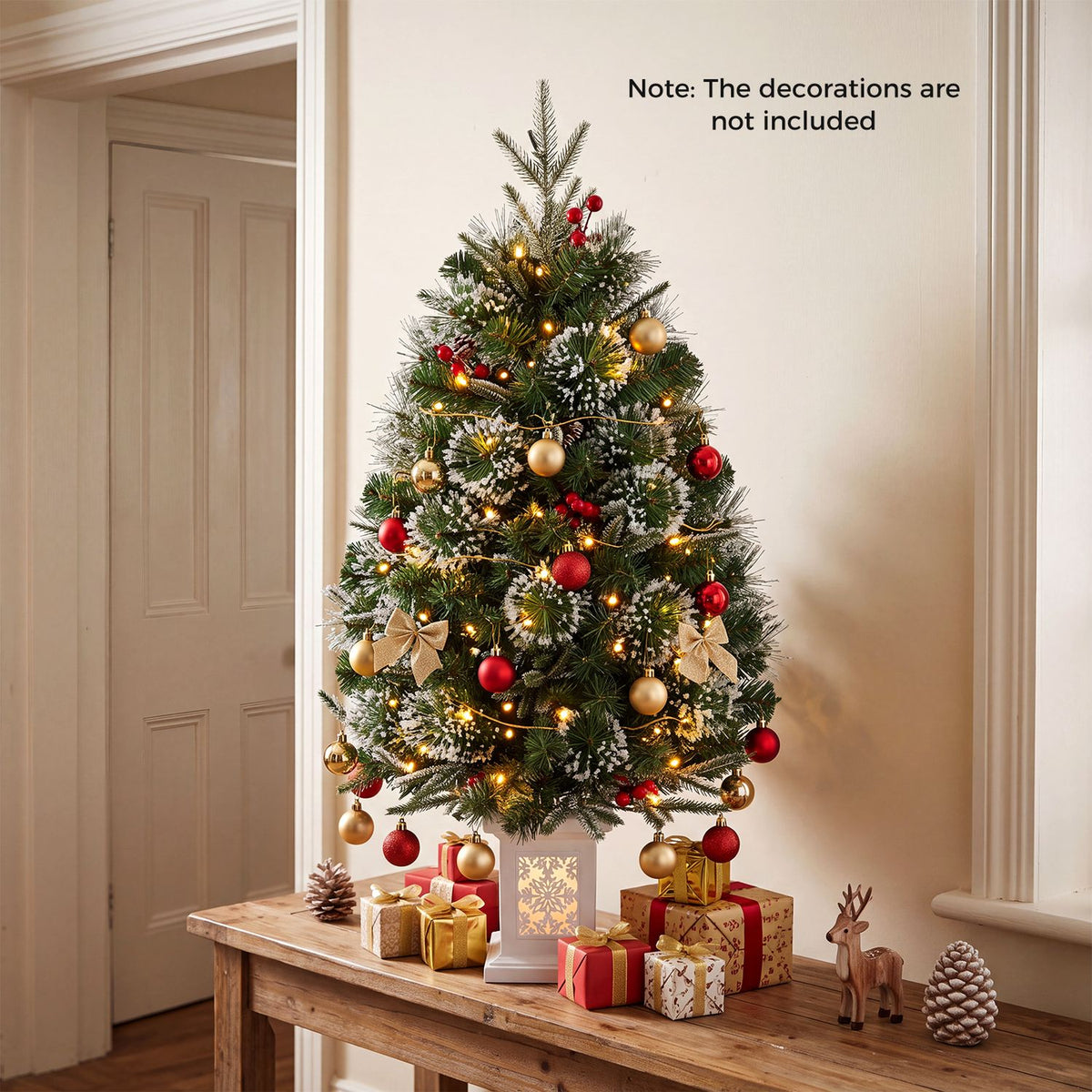 A lit Christmas tree decorated with red and gold ornaments stands on a table among wrapped gifts.