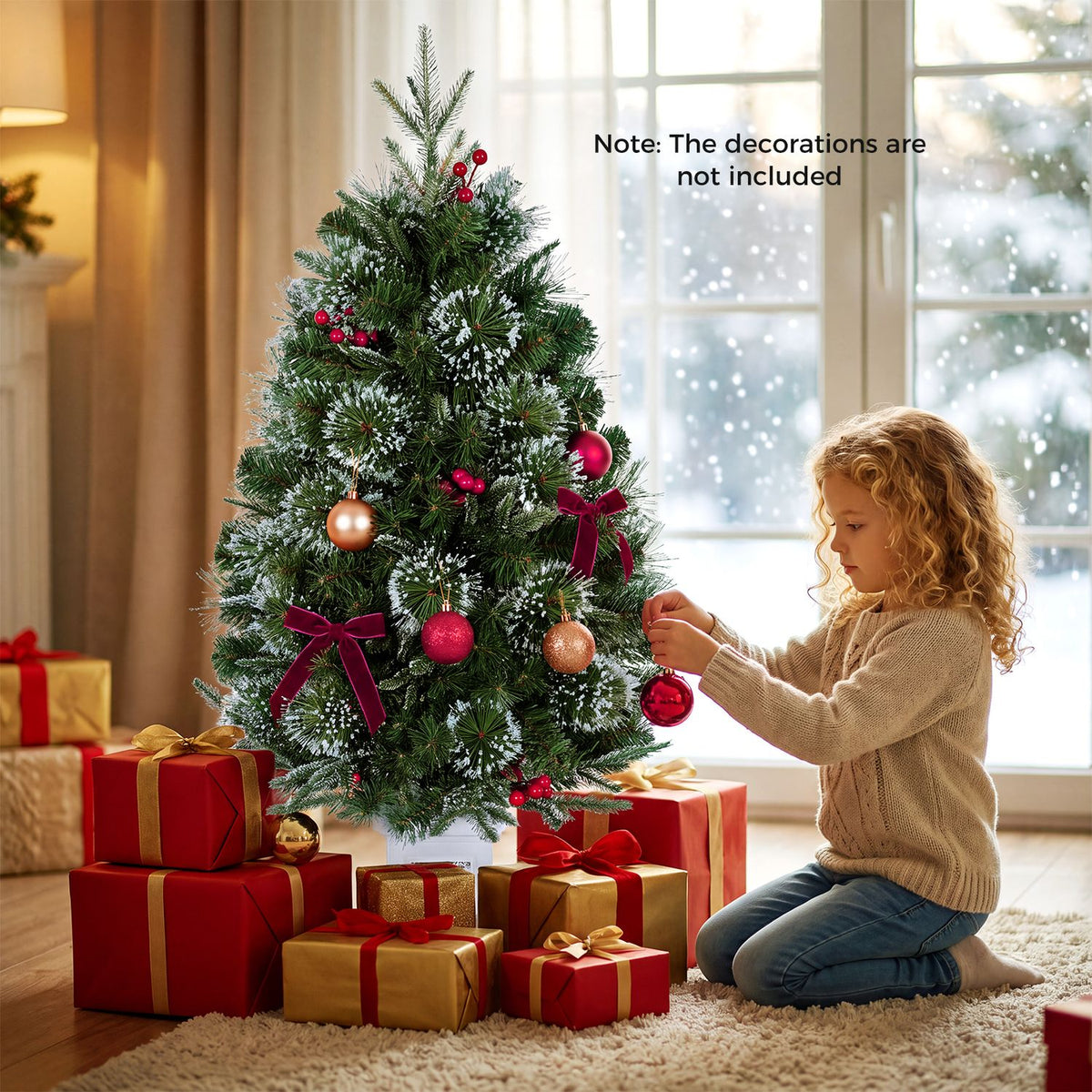 A decorated, lit Christmas tree beside a child arranging an ornament, with wrapped gifts around its base.