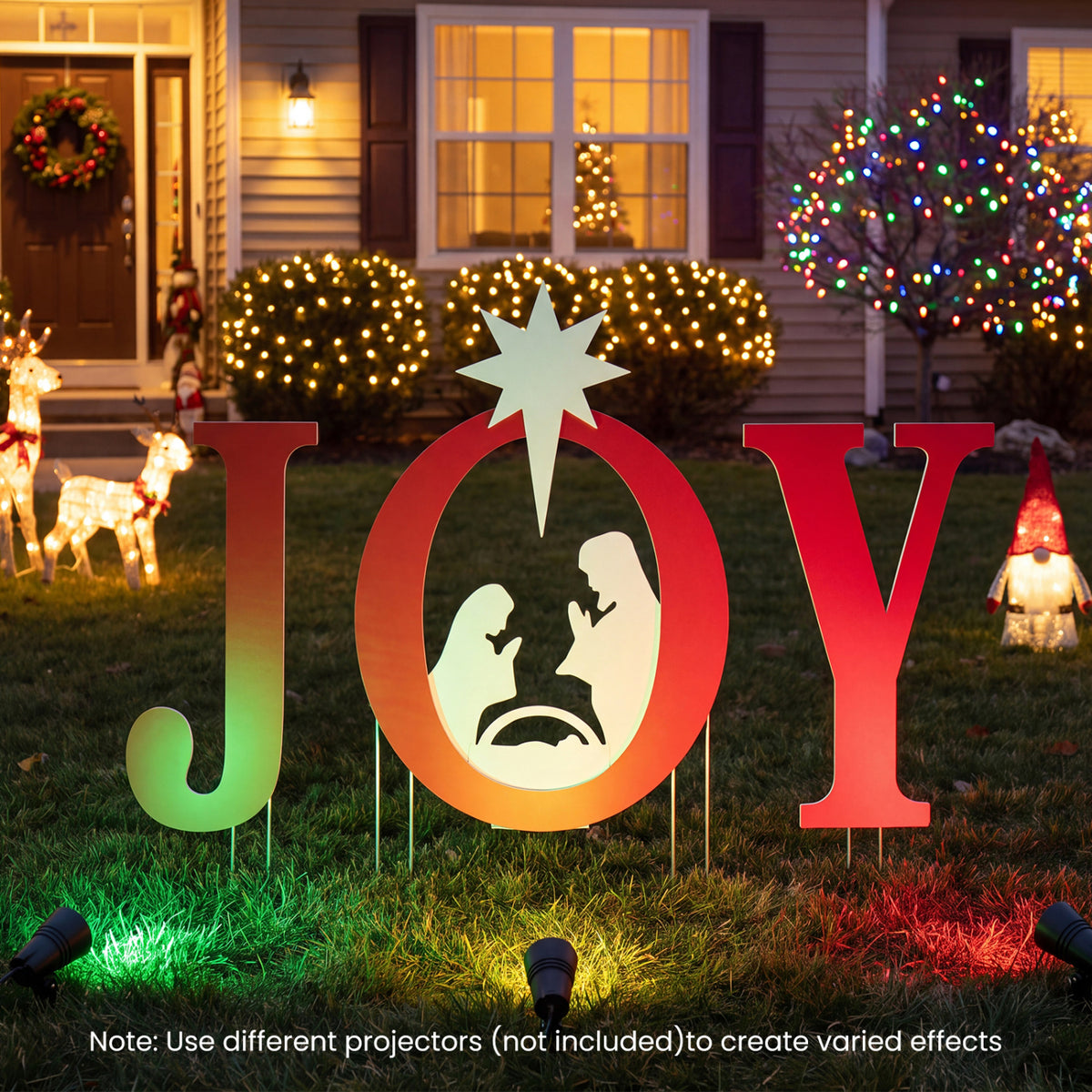 JOY nativity sign in a decorated lawn, lit with red and green effects against a house at night.
