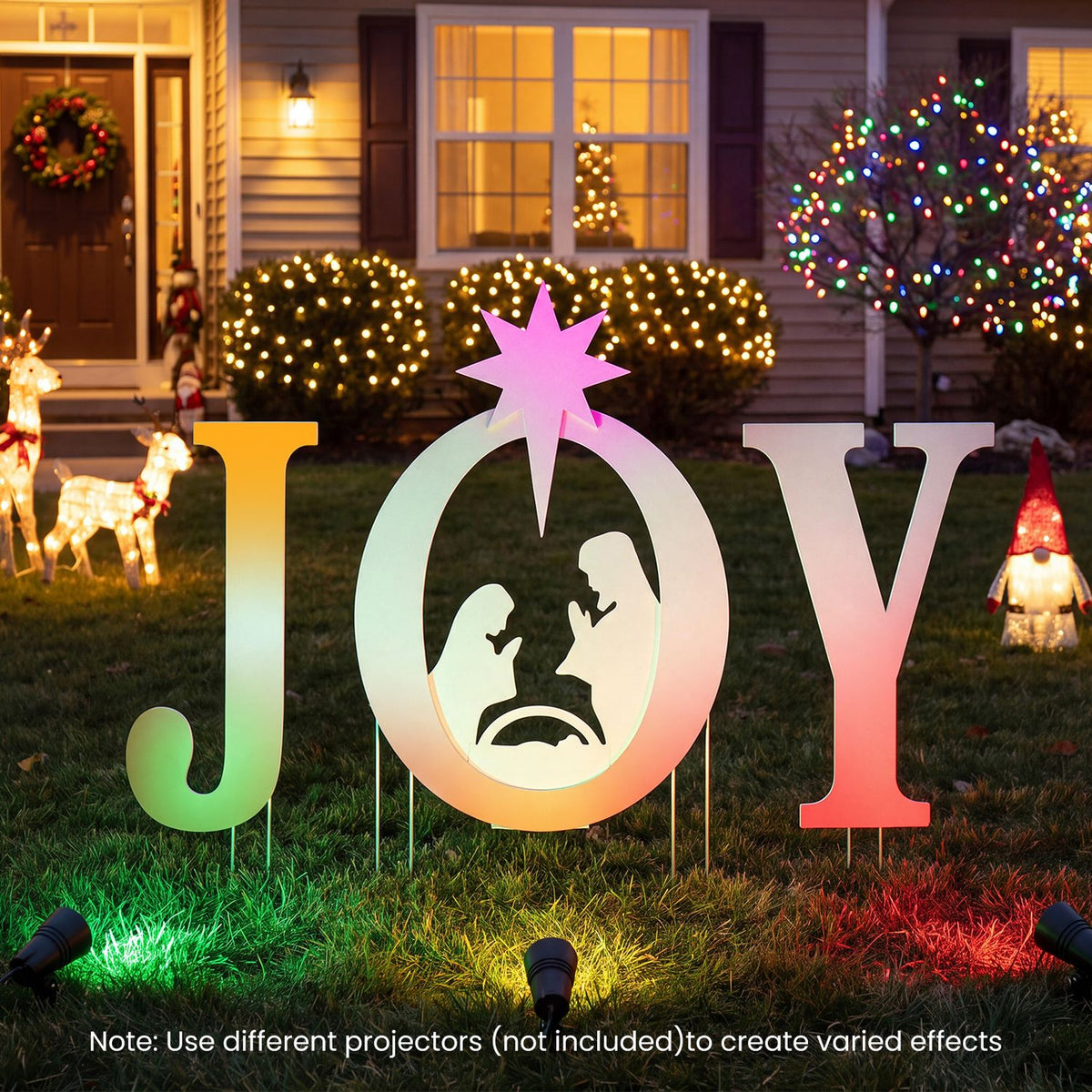 Projector-lit JOY nativity yard sign displayed in a decorated lawn at night