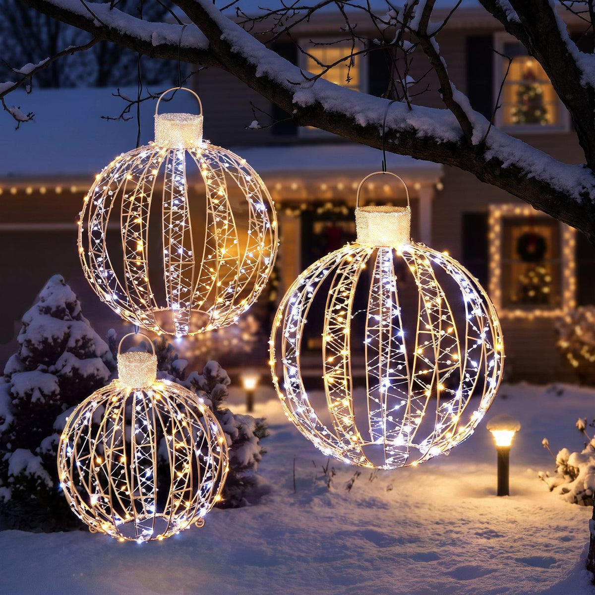 Three illuminated wire-frame balls hang from a snowy tree in a winter yard.