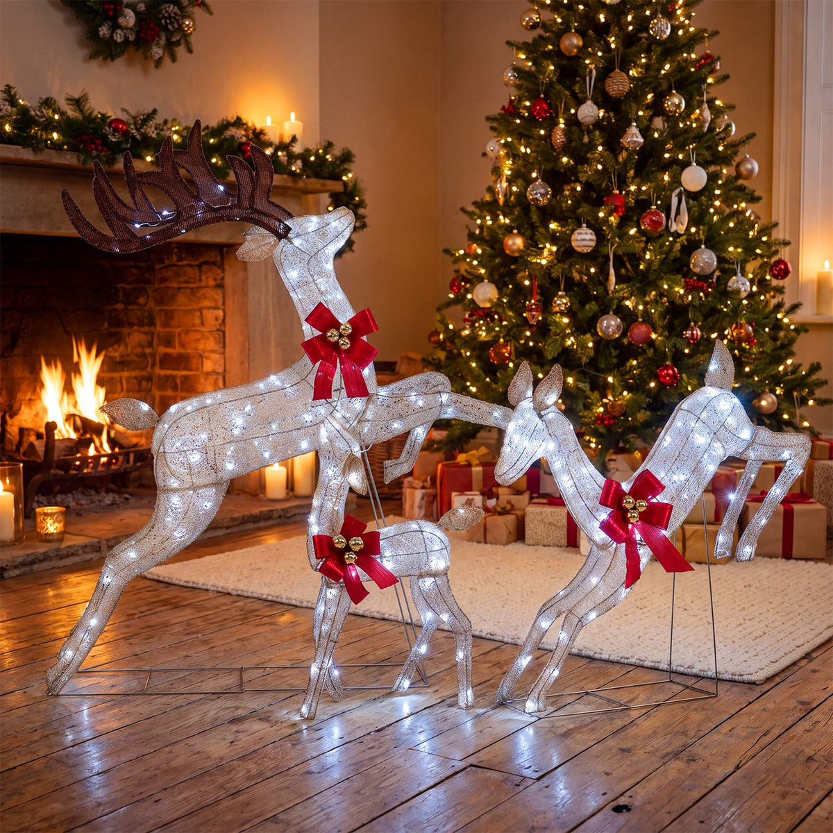 A family of three glowing reindeer is arranged beside a fireplace and decorated Christmas tree.