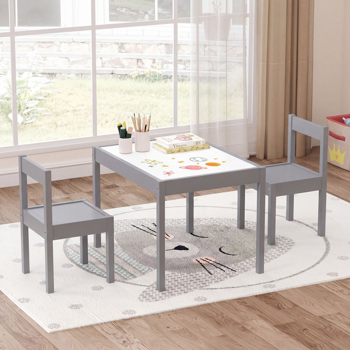 Gray toddler table and two chairs staged by a window, with drawing supplies on the tabletop.