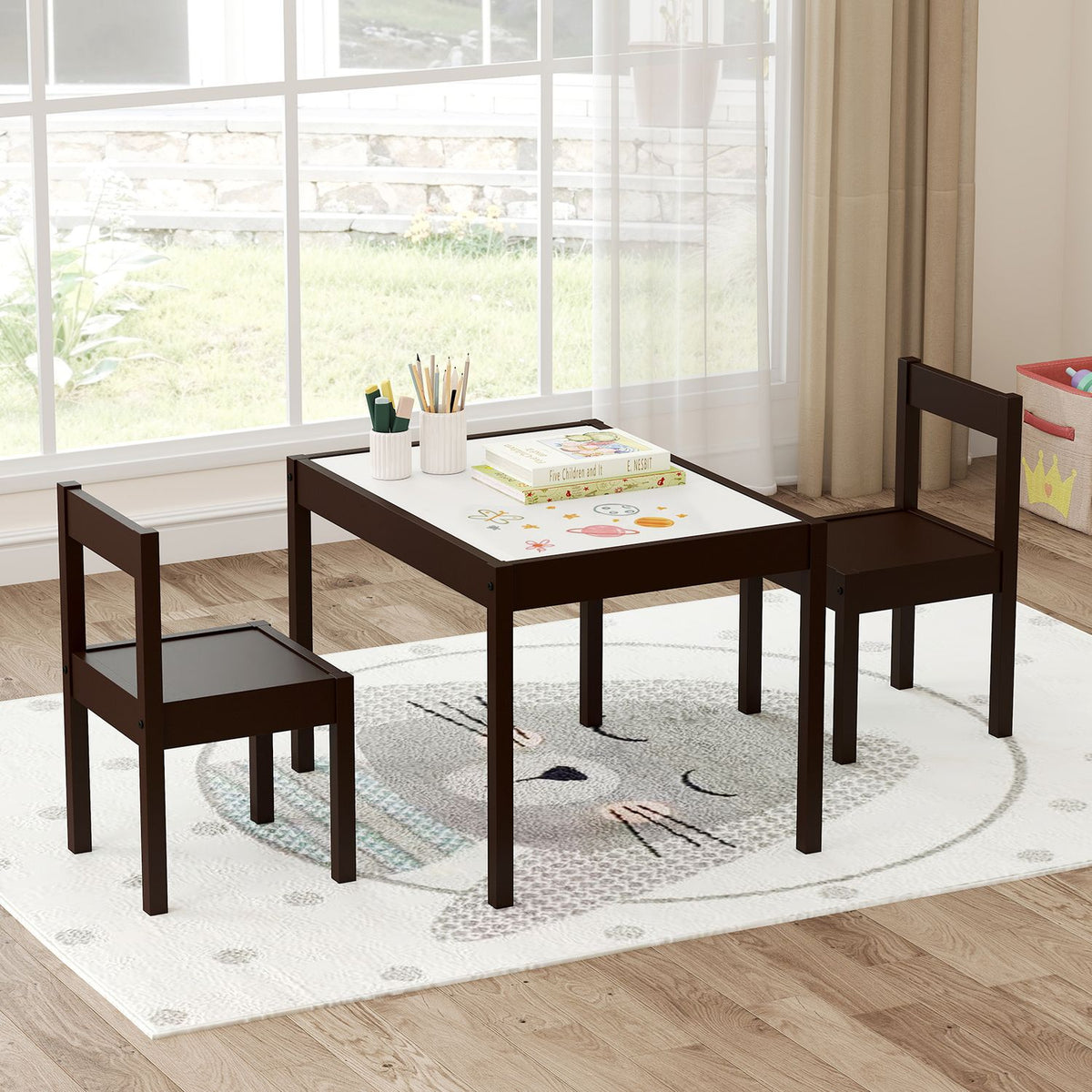 Dark-framed child-size table with two matching chairs arranged on a rug by a window.