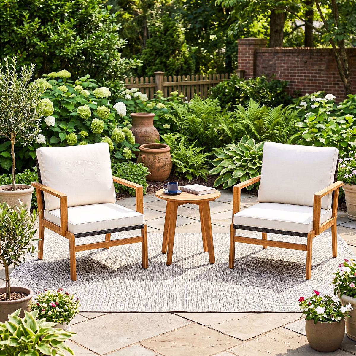 Two cushioned wooden armchairs and a round table on a rug in a leafy garden patio.