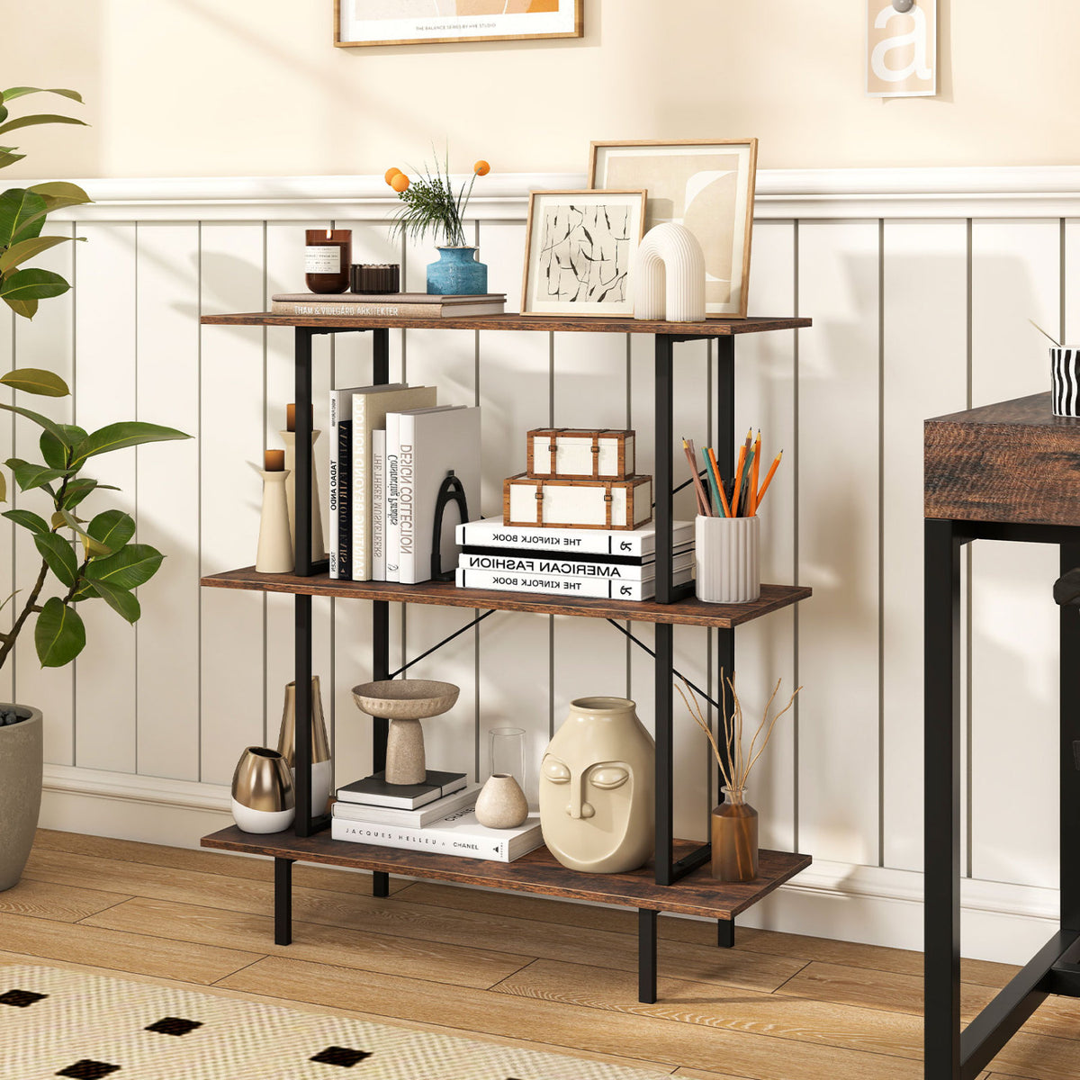 Three-tier bookshelf against a paneled wall, holding books, vases, and small decorative objects.